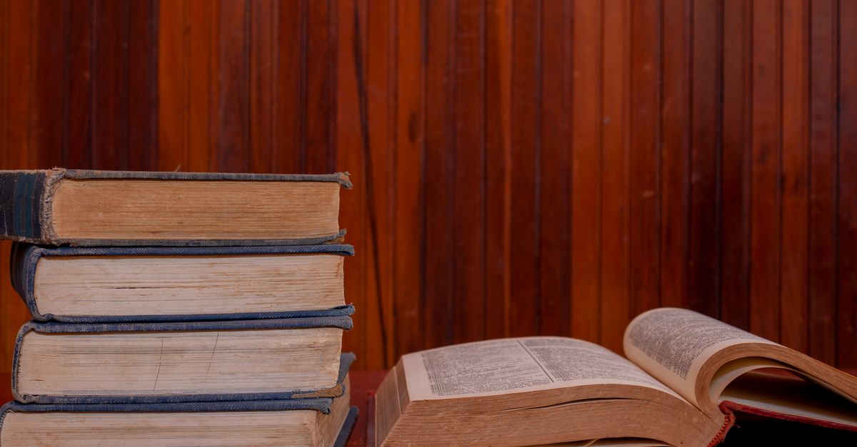 Open books stacked on a wooden table with soft daylight across the pages